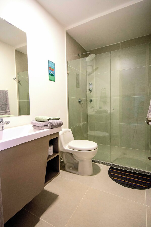 A modern bathroom with a glass-enclosed shower, a white toilet, and a vanity with a mirror.