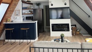 Un espai habitable modern d'estil loft amb cuina, zona de dinar amb tamborets i una llar de foc.