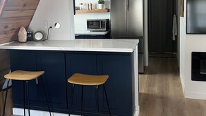 Una cuina moderna amb una illa central, tamborets d'esbarjo, un microones i un frigorífic.