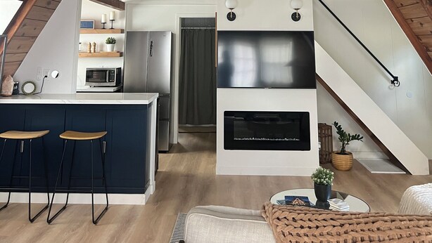 Una cuina moderna amb una illa central, una zona de menjador amb tamboretes i una escala que condueix a un nivell superior.