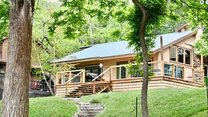 Eine Holzhütte mit einer Steintreppe, die zu einer Terrasse führt, umgeben von Bäumen und einer Rasenfläche.