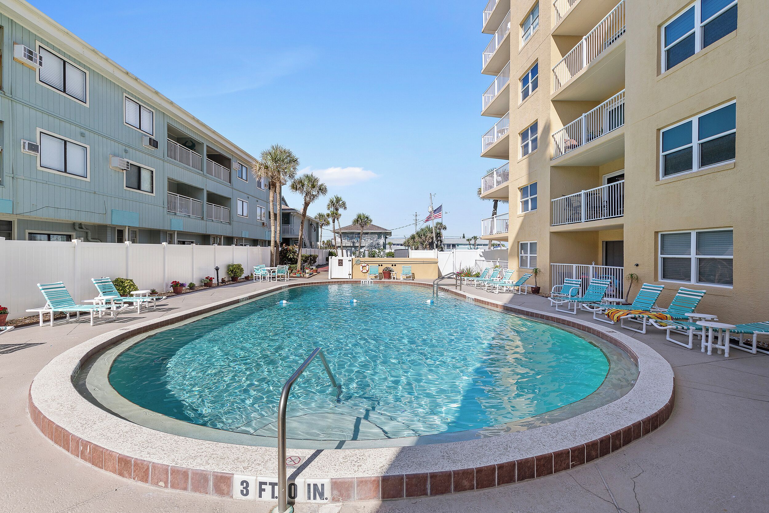 A swimming pool with lounge chairs and a flag, surrounded by multi-story buildings.