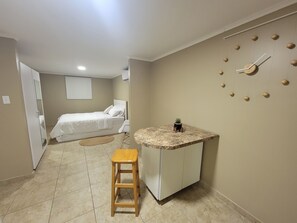 Una stanza compatta con un letto, un angolo cottura, uno sgabello di legno e una sveglia a muro.