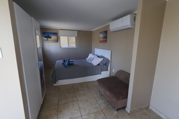 Una camera da letto con un letto, un divano marrone, una finestra e un quadro appeso al muro.
