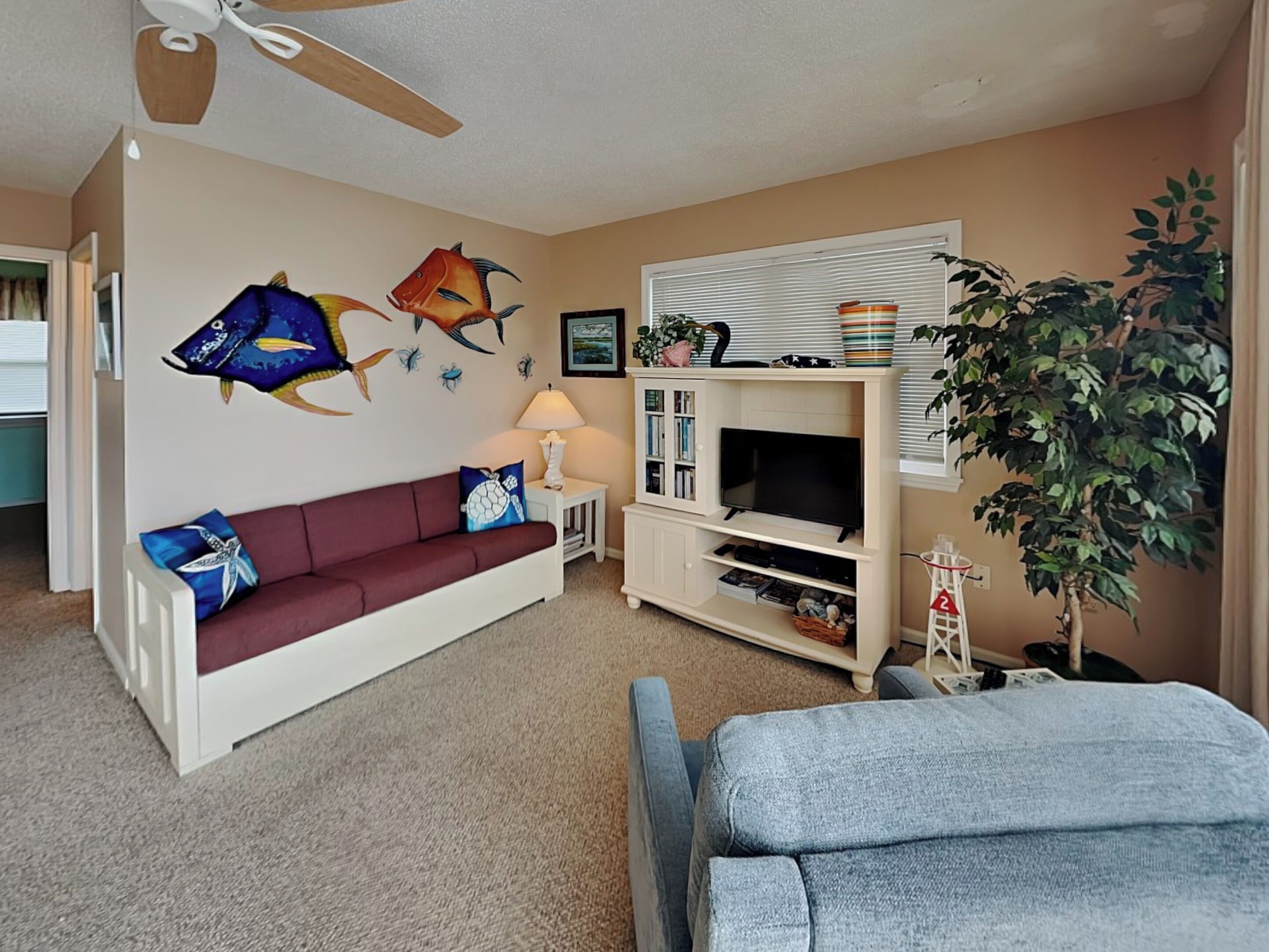 Een woonkamer met een bank, tv-meubel, plafondventilator en een grote potplant.