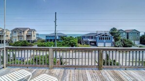 Um deck de madeira com guarda-corpo, com vista para uma praia e casas ao fundo.