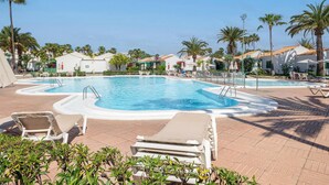 A swimming pool with lounge chairs, palm trees, and white buildings with red accents.