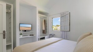 A hotel room with a bed, a desk with a computer, a TV, and a window with a view of the beach.