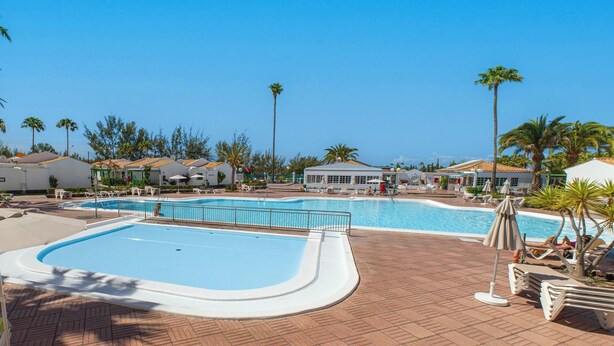 A resort with a large pool area, lounge chairs, and palm trees.