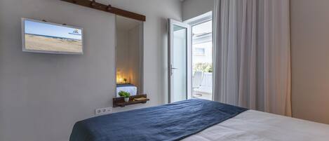 A bedroom with a bed, a mounted TV, a bedside table with a plant, and a view of the outside.
