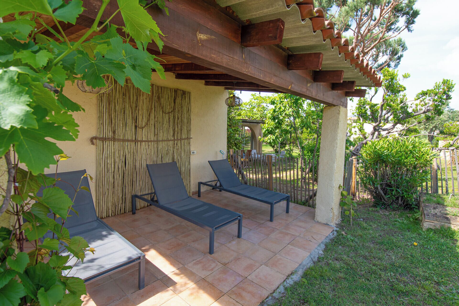 A covered patio area with two lounge chairs and a table, surrounded by a bamboo fence and greenery.