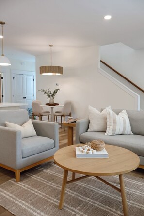 A modern living room with a round coffee table, two sofas, a dining area with chairs, and a staircase.