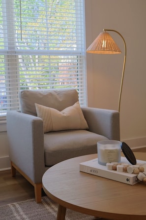 A room with a grey sofa, a round wooden table, a white candle, and a floor lamp.
