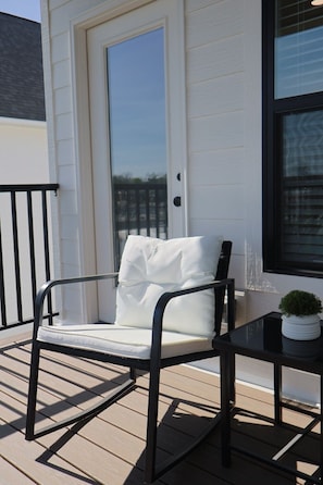 Une chaise avec un coussin, posée sur une terrasse en bois, près d’une porte et d’une fenêtre.