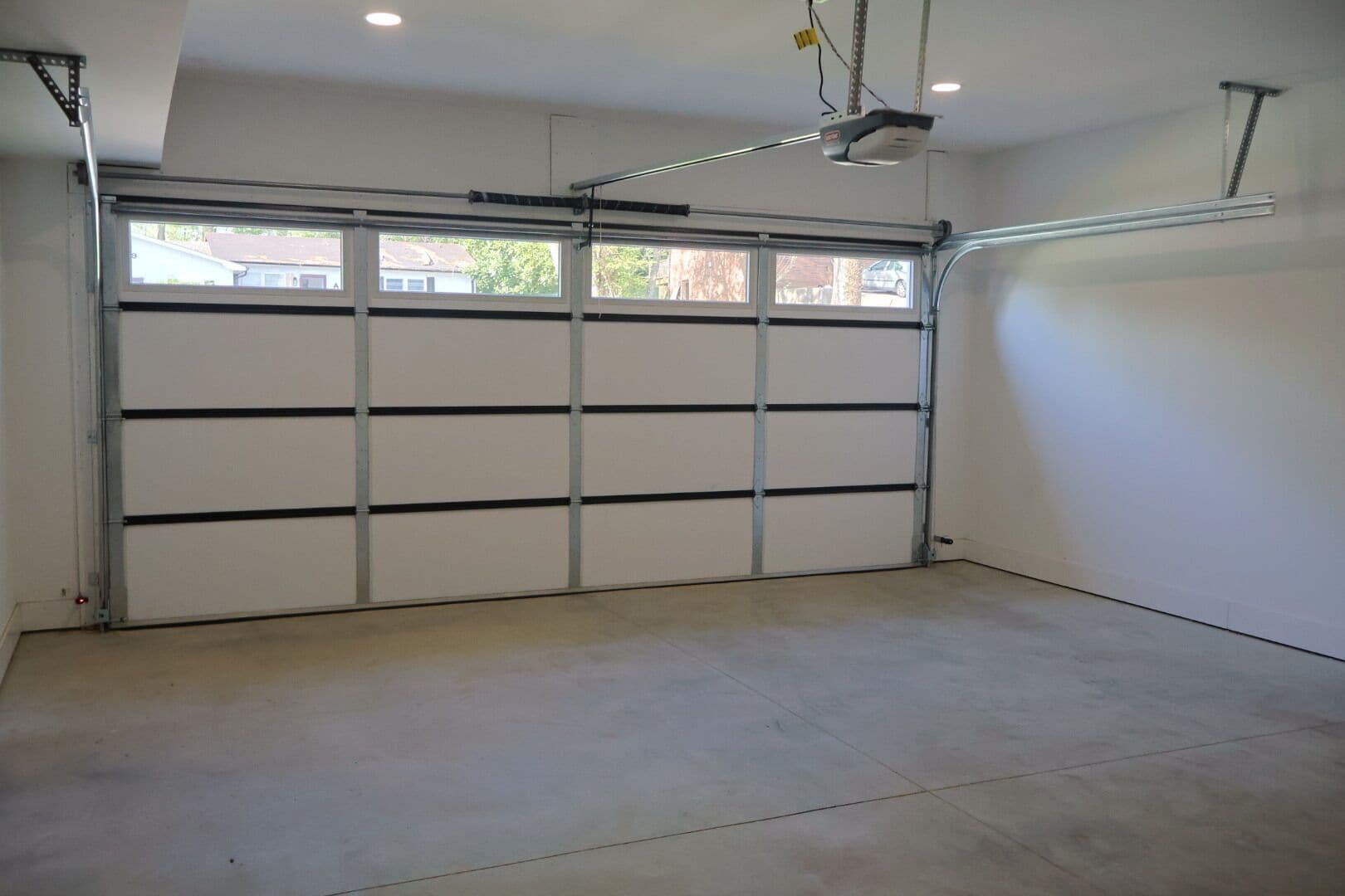 A garage with a metal door, concrete floor, and a ceiling-mounted light fixture.