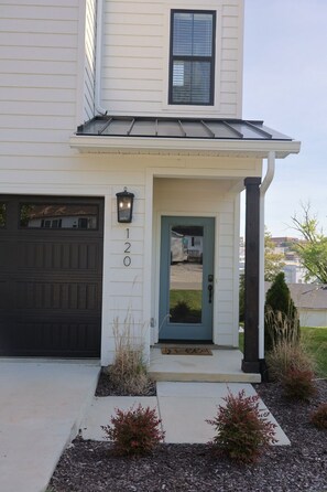A two-story house with a dark garage door, a blue front door, and a small porch with a light fixture.