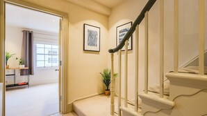 Una escalera con balaustres blancos y un suelo de moqueta color beige que conduce a una habitación con ventana y puerta.