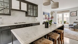 Une cuisine moderne avec des meubles de couleur sombre, un plan de travail en marbre et un îlot central intégré avec des tabourets.