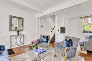 Un salón amplio con techo alto, un espejo grande y una escalera que lleva a un piso superior.
