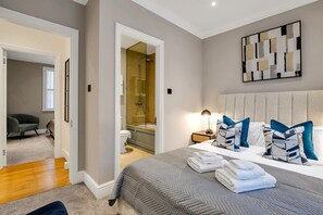A bedroom with a large bed, a nightstand, a wall-mounted abstract art piece, and a view into the bathroom. - Belgravia Luxe 4bed Mews With Roof Terrace (London)