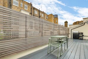 A rooftop patio with a wooden fence, a table, and chairs. - Belgravia Luxe 4bed Mews With Roof Terrace (London)
