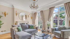 A living room with a grey sectional sofa, a glass coffee table, and a fireplace. - Elegant 5bed House Next to Harrods Knightsbridge (London)