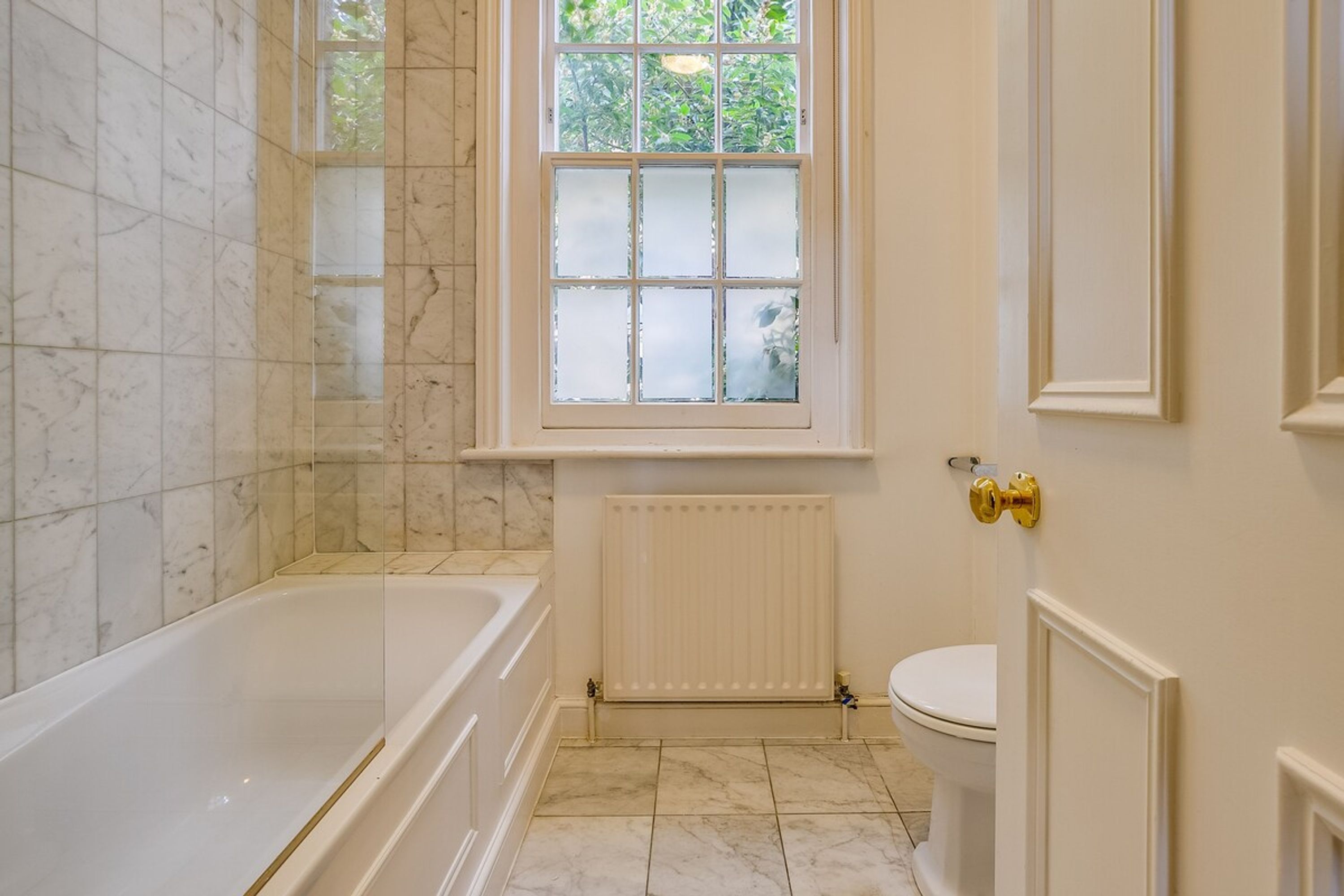 A bathroom with a bathtub, a window, a toilet, and a radiator.