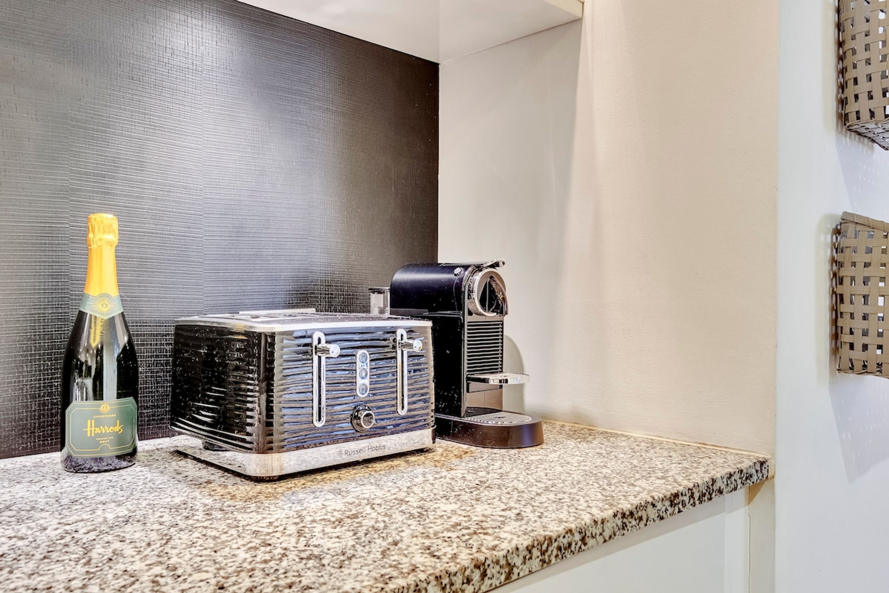 A minibar setup with a bottle of champagne, a Russell Hobbs coffee maker, and a small basket on a granite countertop.