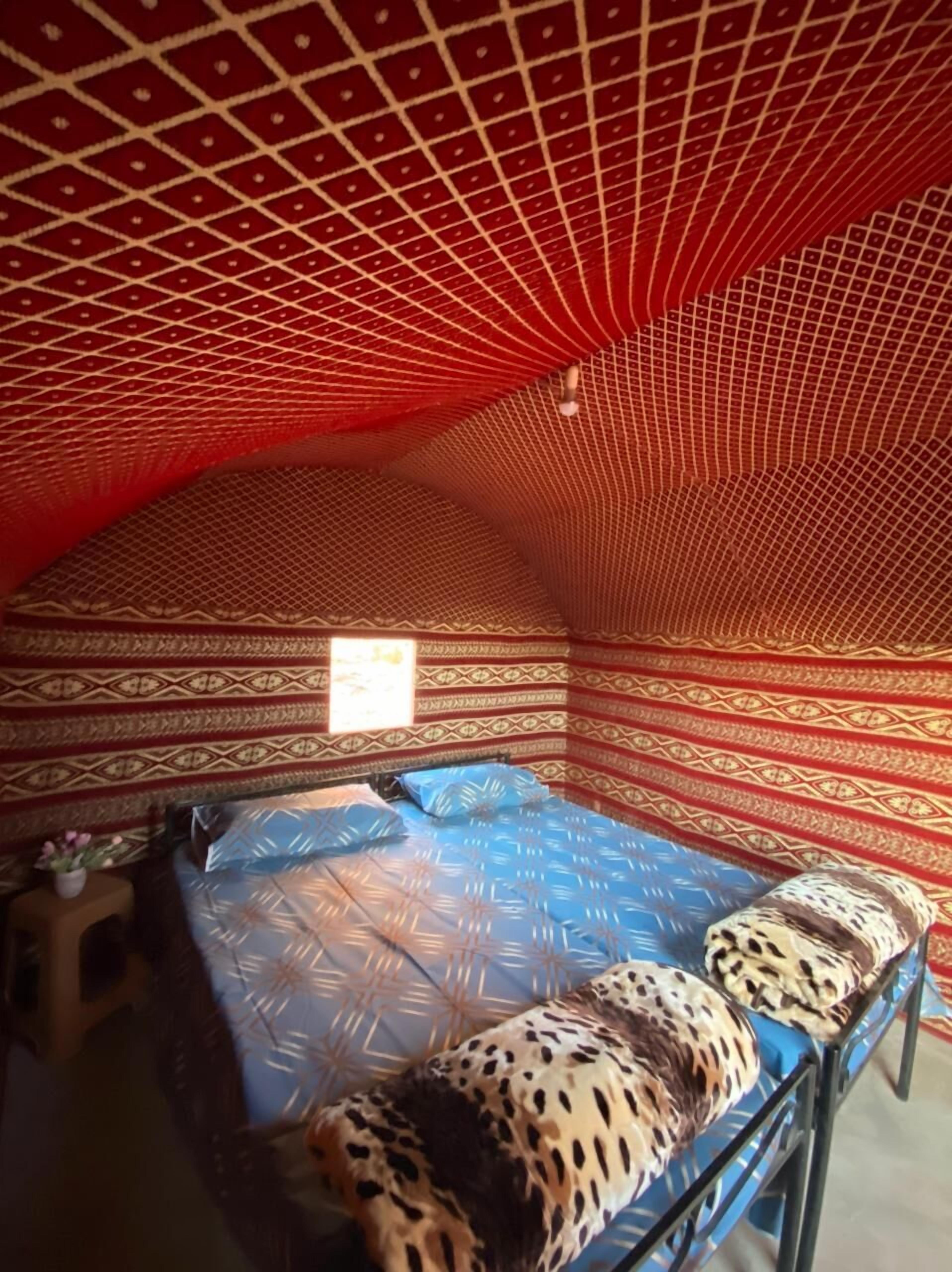 Una habitación con pared de diseño rojo y beige, una cama con colcha azul estampada y un ventanal pequeño.