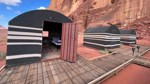 Un campamento en el desierto con varias yurtas, una terraza de madera y un cañón rocoso al fondo.