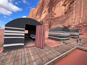 A desert campsite with multiple yurts, a wooden deck, and a rocky canyon backdrop. - Cozy Tent in Wadi Rum (Wadi Rum)