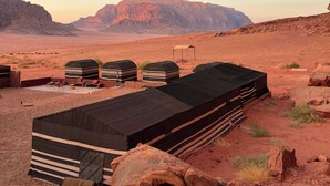 Paisaje desértico con tiendas de campaña y una gran formación rocosa al fondo.