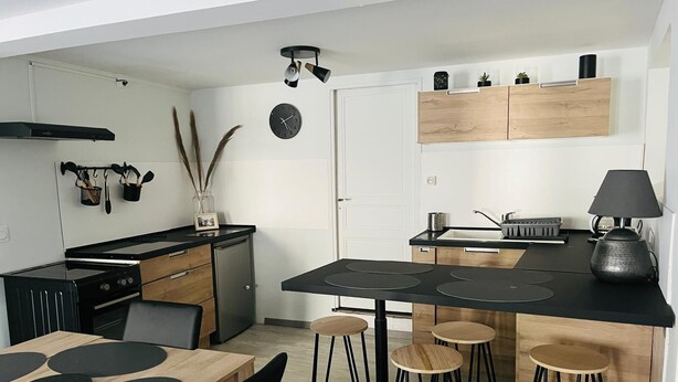 A modern kitchen with a black stove, wooden cabinets, and a black countertop. There are stools and a table with black placemats.