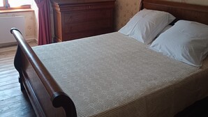 A bedroom with a wooden bed, a nightstand, a dresser, and floral wallpaper.