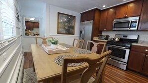 A dining area with a wooden table, chairs, and a central plant. There is a kitchen with modern appliances in the background. - Clean, Bright & Private WHOLE HOUSE 4 YOU. Safe, Centrally Located, Garage (New Britain)