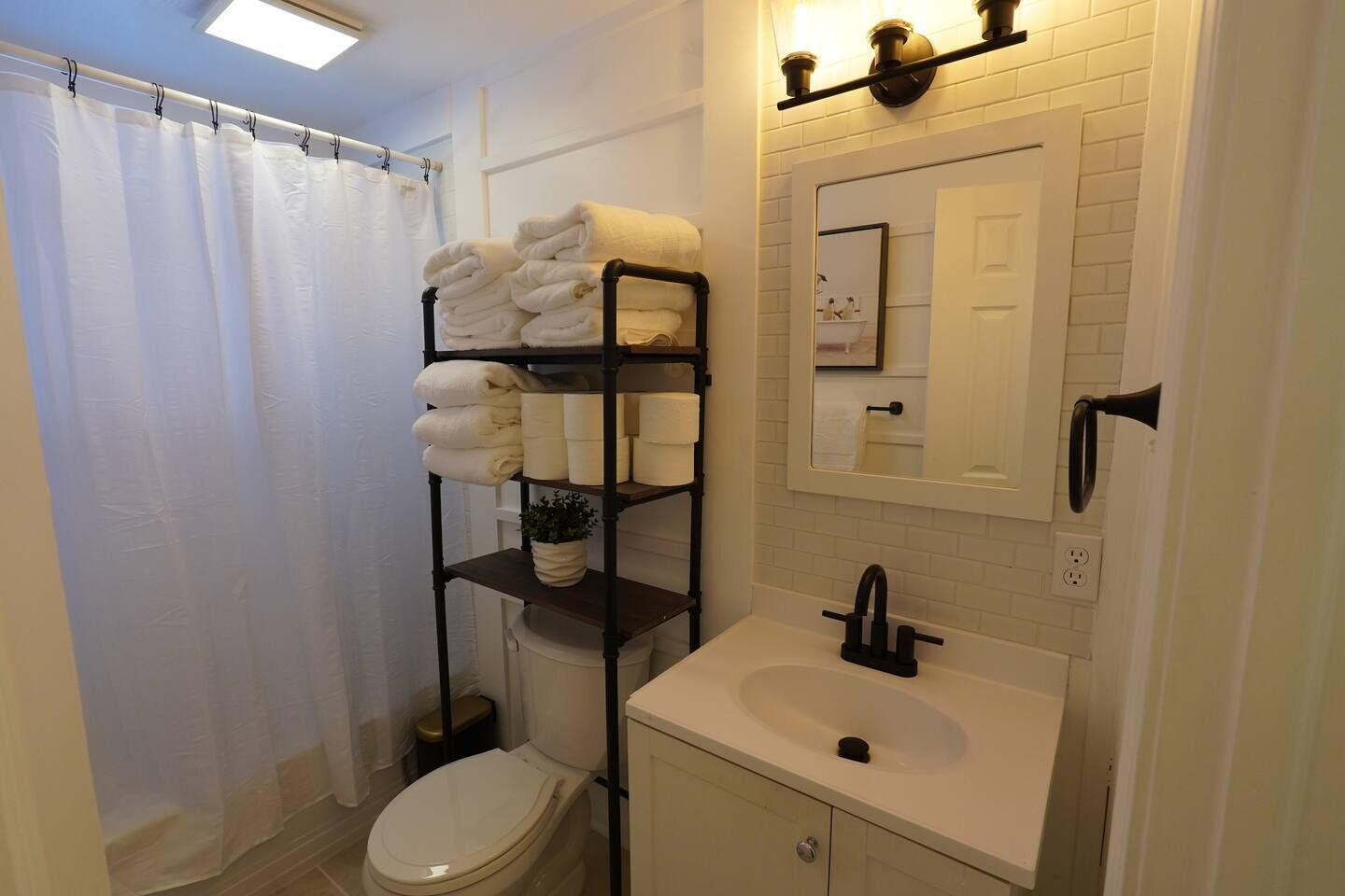 A bathroom with a white toilet, a sink with a black faucet, a towel rack with folded towels, a mirror, and a shower curtain.