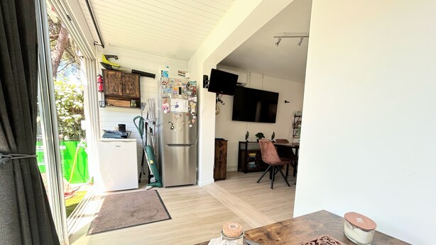 A modern kitchen with a stainless steel refrigerator, a dining area with a wooden table and chairs, and a television mounted on the wall.