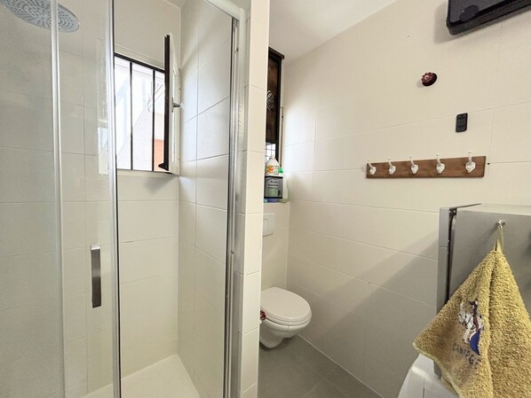 Un baño con cabina de ducha de vidrio, inodoro y toallero con una toalla.