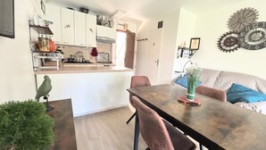 A modern kitchen with white cabinets, a dining table with chairs, and a living area with a sofa and decorative wall art.