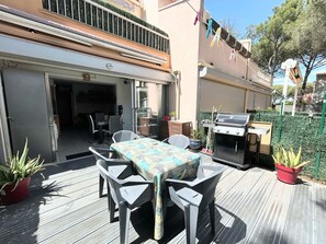 En uteplats med ett bord och stolar, en grill och krukväxter.