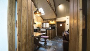 A rustic interior with a wooden dining area, stone flooring, and a kitchen with a stone wall. - Lavender - Barn Conversion - Blossom Farm (Haverfordwest)