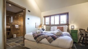 A bedroom with a large bed, a window, a green cabinet, and a wooden door leading to a bathroom. - Lavender - Barn Conversion - Blossom Farm (Haverfordwest)