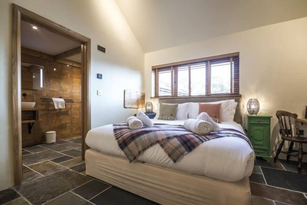 A bedroom with a large bed, a window, a green cabinet, and a wooden door leading to a bathroom.