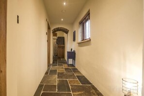A hallway with a stone floor, a wooden door at the end, and a small table with a lamp. - Lavender - Barn Conversion - Blossom Farm (Haverfordwest)
