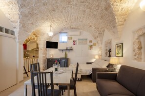 Una habitación acogedora con techo de piedra, una mesa de comedor con sillas, un sofá y un televisor montado en la pared.