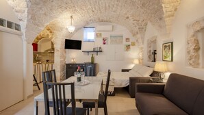 Ein gemütliches Zimmer mit Stein Decke, einem Esstisch mit Stühlen, einer Couch und einem an der Wand befestigten Fernseher.