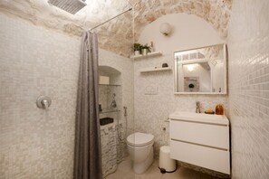 A bathroom with a shower, toilet, and sink, featuring a stone wall and tiled floor.