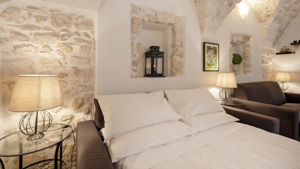Ein Schlafzimmer mit Steingemäuer, einem Bett mit weißen Leinentüchern, zwei Nachttischen mit Lampen und einem kleinen Fenster.