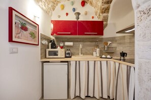 A kitchen with a white refrigerator, a microwave, a sink, and a red cabinet. There is a painting on the wall and a curtain over the sink.