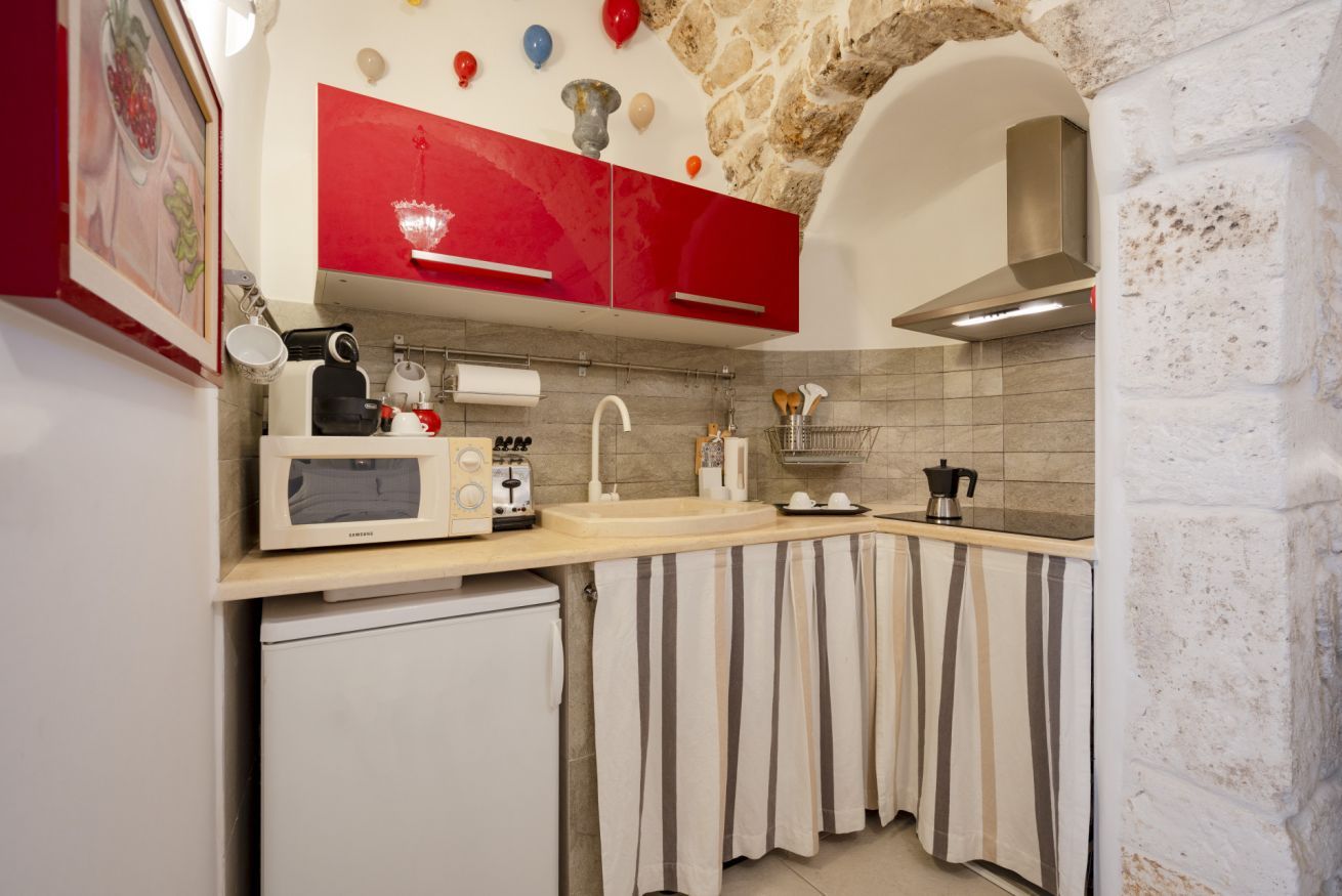 A kitchen with red cabinets, a microwave, a coffee maker, and a small refrigerator.